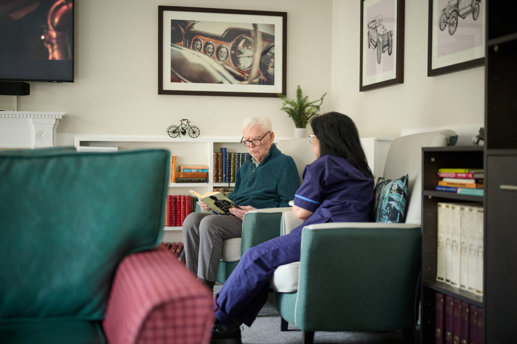 female nurse sitting in the communal lounge with a resident male reading together