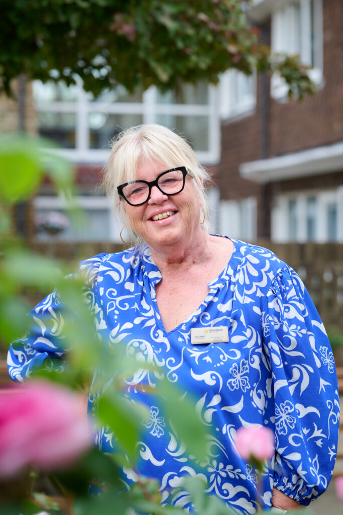care home manager headshot in the garden wearing a blue flower blouse and black thick glasses