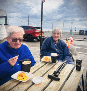 two female residents of upper mead care home enjoying coffee and chips outside at Brighton Beach