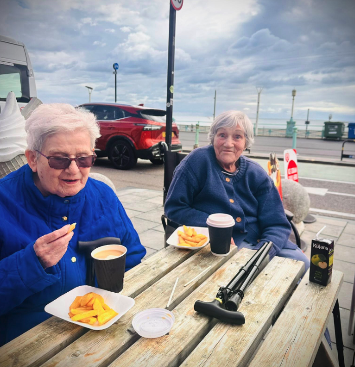 two female residents of upper mead care home enjoying coffee and chips outside at Brighton Beach